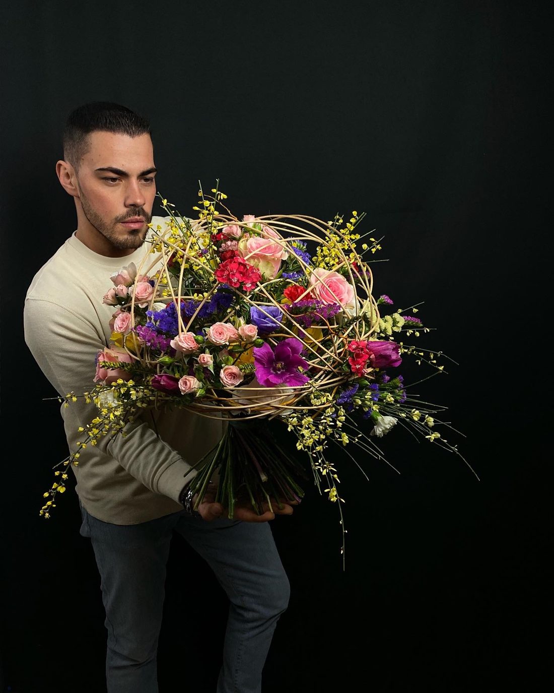 Mario Garofalo regge un mazzo legato con una struttura sferica in rami chiari, rose, anemoni, statice e ginestra.