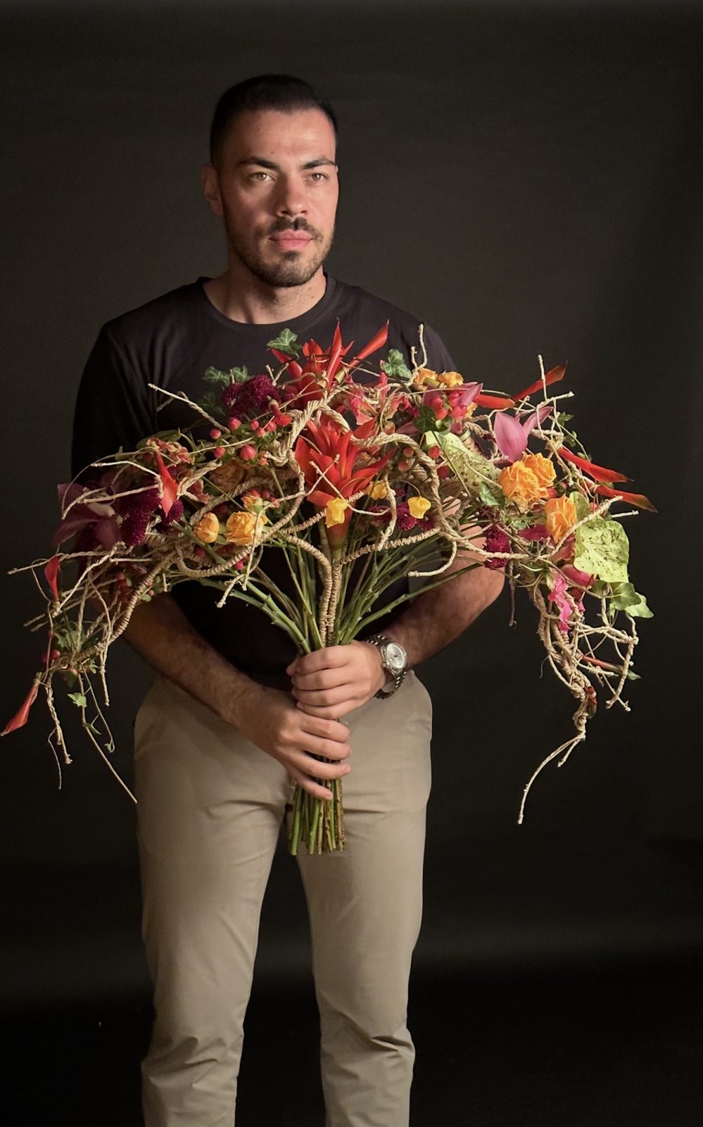 Mario Garofalo regge un grande mazzo legato con una struttura in corda intrecciata, fiori rossi, arancioni e bacche.