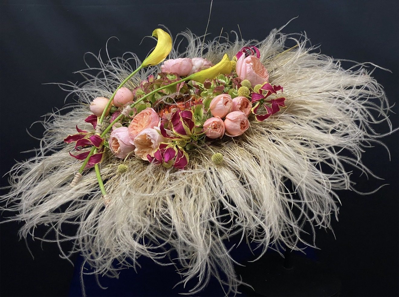 Composizione di Mario Garofalo con una base di fibre chiare, rose, calle gialle e fiori rosa.