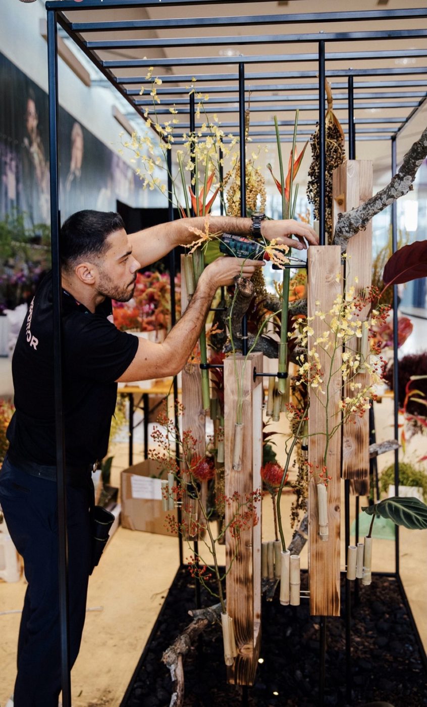 Mario Garofalo al lavoro su una grande installazione floreale con travi di legno, bambù, orchidee e bacche.